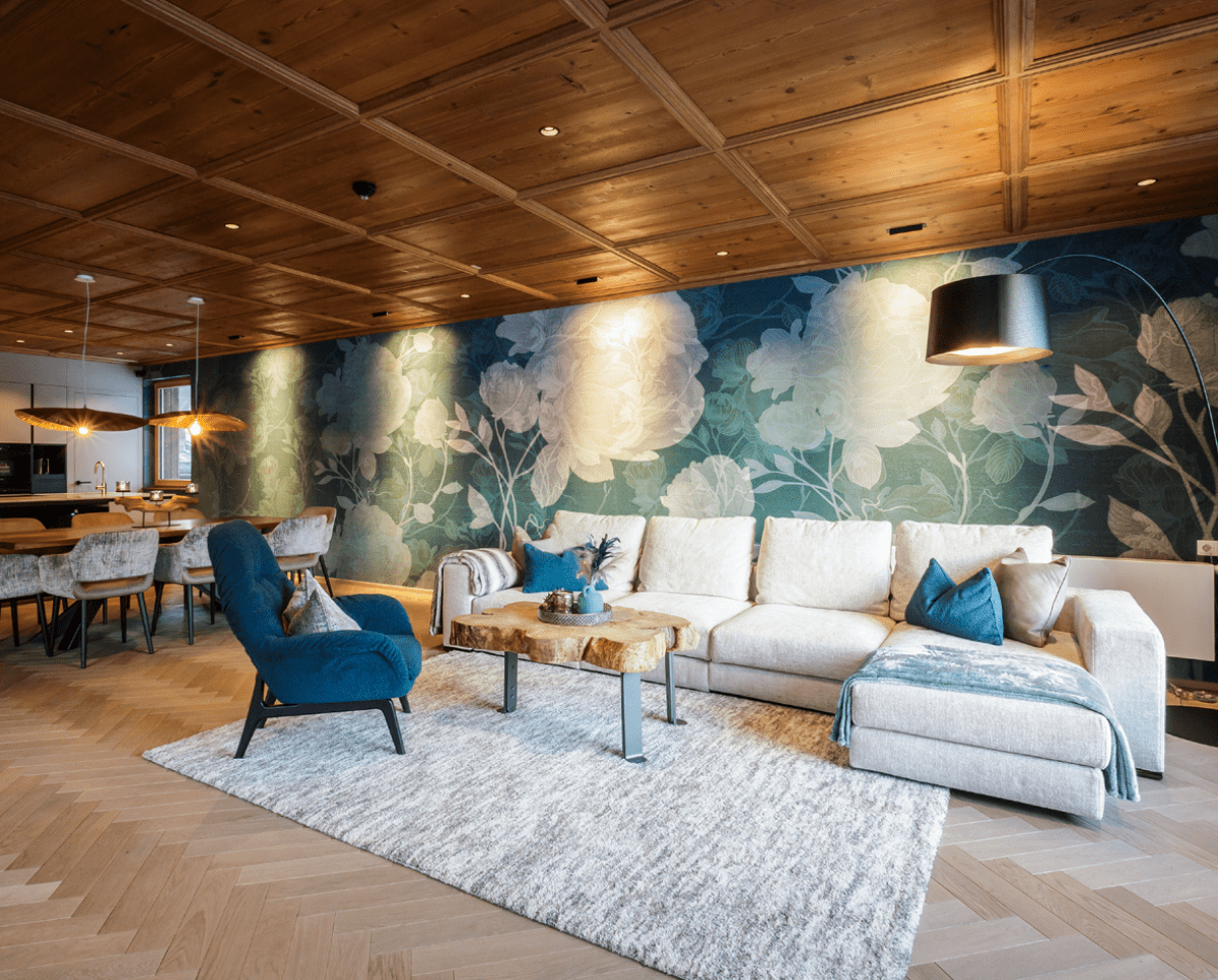 Helle Wohnlandschaft in modernem Wohnzimmer mit Blumentapete, Holzdecke und verschiedenen blauen Textilelementen.